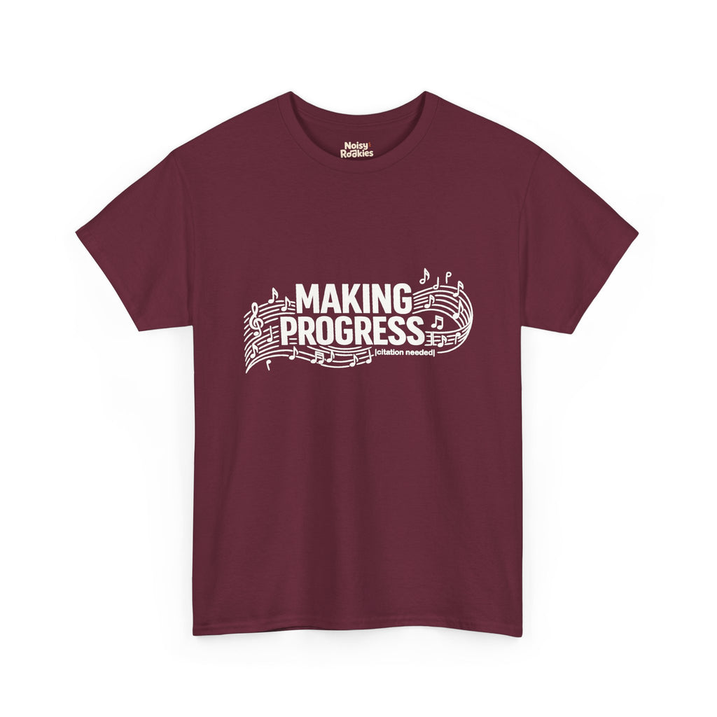 White t-shirt design reading MAKING PROGRESS with a small "citation needed" tag, woven through a flowing musical staff with a treble clef and scattered notes.